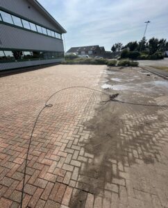 Mid-clean pressure washing of block paving at a commercial site in Worthing showing stark contrast between cleaned and uncleaned areas